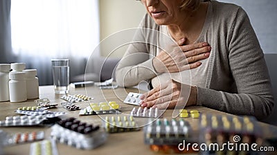 Lonely old woman suffering heart problem, feeling unwell, looking for pills Stock Photo