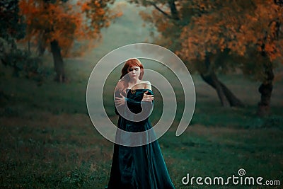 Lonely sad girl walks alone in terrible dark dangerous forest in long green emerald dress and raincoat with open Stock Photo