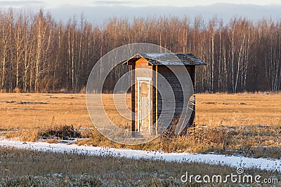 Lonely small building- toilet barn in a field against the backdrop of the forest in winter Stock Photo