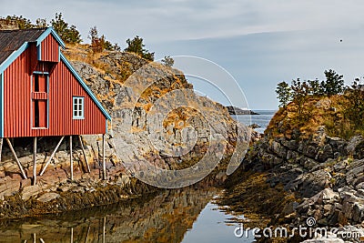 Lonely small fishing house of red color on the coast on Lofoten Islands, classic norwegian landscape, rocky coast with Stock Photo