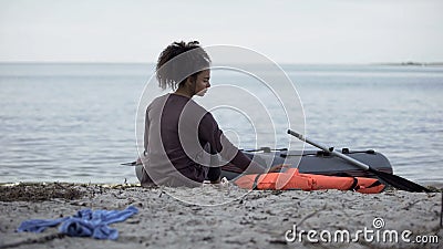 Lonely teenage girl sitting near boat, shipwreck survivor on desert island Stock Photo