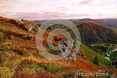 Lonely tourist in an orange vest sits at top of a hill in a natu Stock Photo