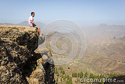 Lonely tourist on pink t shirt sitting on edge of cliff rock Stock Photo