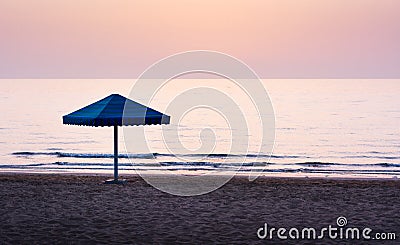 Lonely umbrella on empty beach at dusk Stock Photo