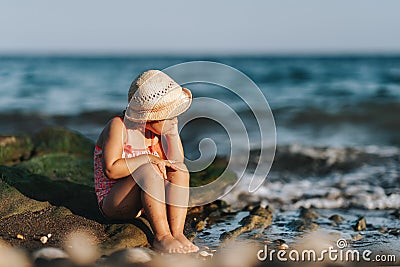 Lonely unhappy girl sitting on a rock on the beach. Stock Photo