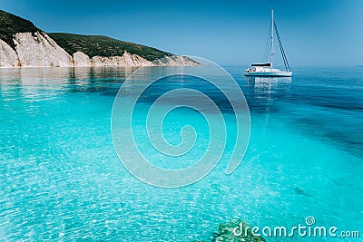 Lonely white sailing catamaran boat drift on calm sea surface. Pure shallow azure blue bay water of a beautiful beach Stock Photo