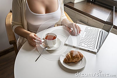 Lonely woman freelancer enjoying having breakfast with cup of coffee working on laptop sitting near window in cafe at morning. Stock Photo