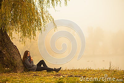 Lonely woman having rest under the tree near the water in a foggy autumn day Stock Photo