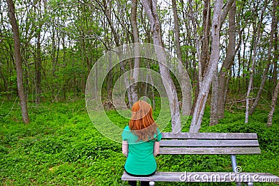 Lonely woman rear view looking to forest sitting on bench Stock Photo