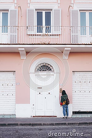 Lonely young female standing in front of a pink and white painted building with open windows Stock Photo