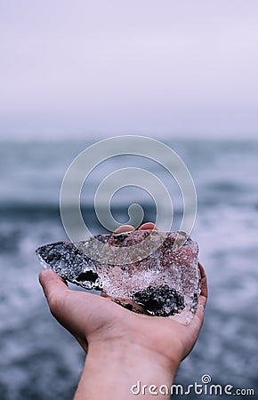 Lonesome male solo traveler holding a piece of crystal-white ice covered with blackest Icelandic soil Stock Photo