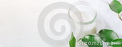 Long Banner for Organic Cosmetics Wellness White Candle in Glass Jar Fresh Tree Branches with Green Leaves on Wood Background. Spa Stock Photo