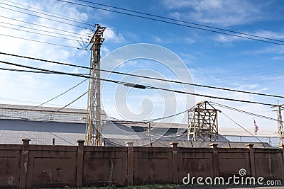 Long dark wall separating a large industrial facility from the street, heavy electrical power lines before a bright blue sky with Stock Photo