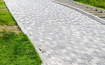A long descent covered with gray paving slabs. The ramp is paved with concrete tiles. Wheelchair and bicycle accessibility concept Stock Photo