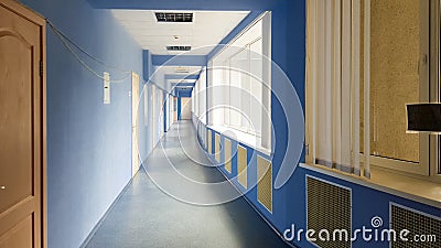 Long empty corridor without people in a hospital with blue walls, wooden doors and windows. Sun rays from the windows in a long Editorial Stock Photo