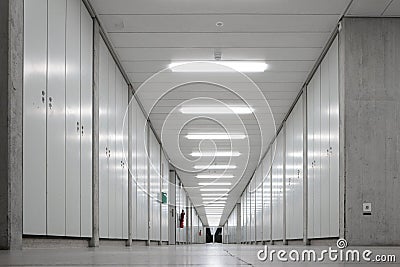 Long empty illuminated interior hallway. Vanishing perspective, bright neon lights, vertical cabinets lined side wall. Underground Stock Photo