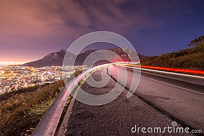 Long exposure of car driving around a bend with Table Mountain in the background in Cape Town as seen from Signal hill. Stock Photo