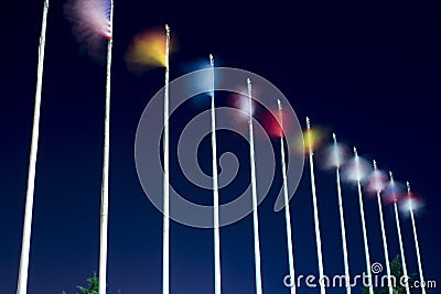 Long exposure flags. Waving flags on the wind at night. Different countries flags are on the pillars Stock Photo