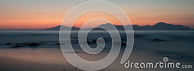 A long exposure of the sea at golden hour, as the sun sets behind a mountain. Stock Photo