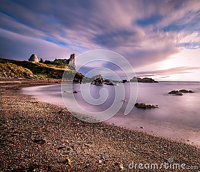 Long exposure of seascape featuring the old vintage ruins of Dunure Castle with wispy smooth clouds and ocean Stock Photo