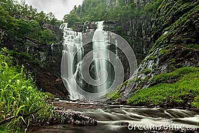 Long exposure shot of a Skjervefossen waterfall in a valley emerging from the forest in Bergen area Stock Photo