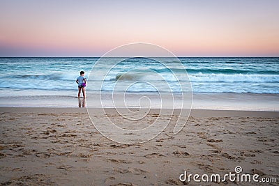 Long exposure sunset mage of young girl standing on a beach with waves. Stock Photo