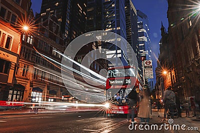 Long exposure of traffic lights with red bus on stop at the road. City buildings in the background at night Editorial Stock Photo