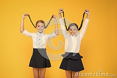 Long hair growth stimulant. Cute small children holding long hair braids on yellow background. Adorable little girl Stock Photo