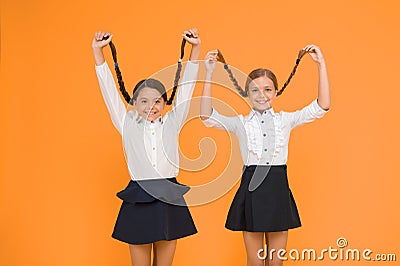 Long hair growth stimulant. Cute small children holding long hair braids on yellow background. Adorable little girl Stock Photo