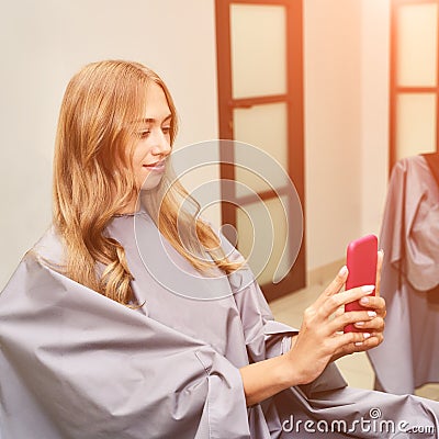 Long hair procedure at salon. Woman with smartphone. Adult female person Stock Photo