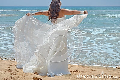 Long-haired brunette bride straightens her dress standing on the sand, girl looks up at the sky on beach on the Indian Ocean. Wedd Stock Photo