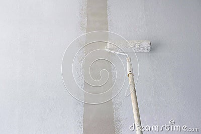 Long handle roller brush applying primer white paint on cement wall Stock Photo