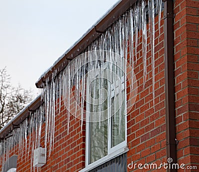 Long icicles hang from the gutter of a house. The roof is covered in snow and it`s still snowing Stock Photo