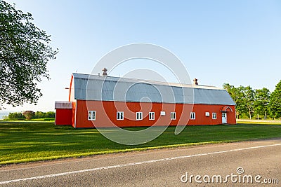 Long metal-clad orange barn with grey roof seen close to the road during a beautiful sunny spring morning Stock Photo