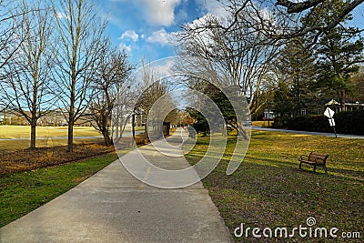 A long paved bike trail with a yellow line in the middle with a woman running in a red top and lush green trees Stock Photo