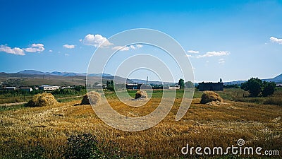 A long shot of hay bales gathered together on a wheat field on a hot and Sunny summer day, far visible houses, mountains and very Stock Photo