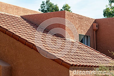 Long slanted adobe style roof with red tiles and orange stucco exterior with back and front yard trees in a neighborhood Stock Photo