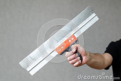 A long spatula in the outstretched arm of the master. Home repair tool in the hand of a handyman. Construction or repair concept Stock Photo