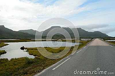 Long strait road with ocean water on sides and mighty mountains in summer Stock Photo