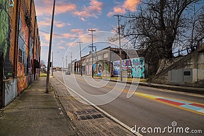 A long street with tall telephone poles and colorful wall murals and bare winter trees and tall curved light posts with blue sky Editorial Stock Photo