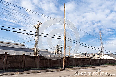 Long wall between street and industrial steel mill, power lines, blue sky with clouds Stock Photo