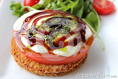 White dish with thick fried tomatoes with cheese slices and drizzle of savory dressing Stock Photo