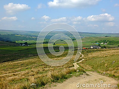 A long winding footpath running downhill in stoodley moor in yorkshire with fields and farms in the distance with pennine hills Stock Photo