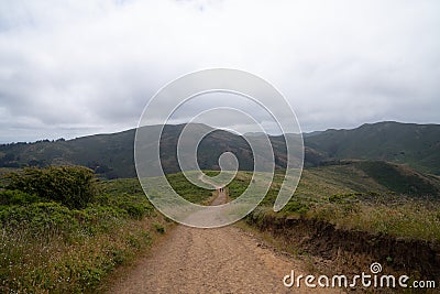 Long, winding hiking trail leading to mountains with two hikers marching into distance Stock Photo