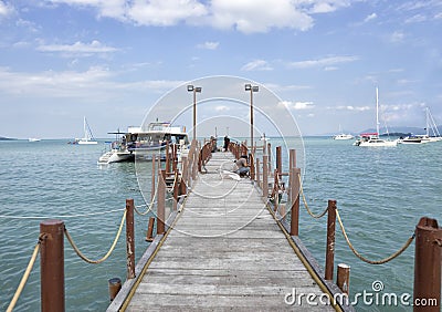 A long wooden pier at the ferry from Koh Samui to Phangan Island in Thailand. A ferry-boat departs from the pier Stock Photo