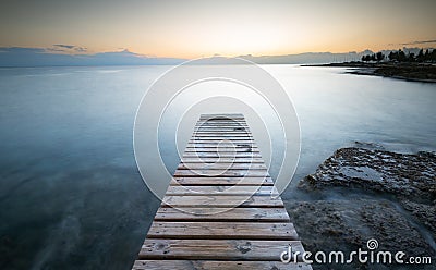 Long wooden pier in the sea at sunrise Stock Photo