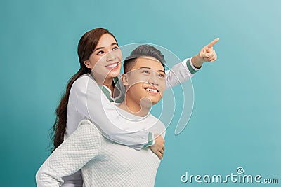 Look Here. Vertical portrait of happy couple pointing finger at side, man giving his lady piggyback ride Stock Photo