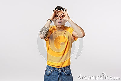 Look at that prices. Amazed and surprised fascinated asian millennial man in yellow t-shirt, make circles over eyes like Stock Photo