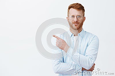 Look there now. Portrait of handsome redhead male with beard in eyewear and shirt pointing at upper left corner and Stock Photo