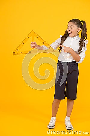 Look at the triangle with two equal sides. Happy little schoolgirl holding triangle on yellow background. Cute small kid Stock Photo
